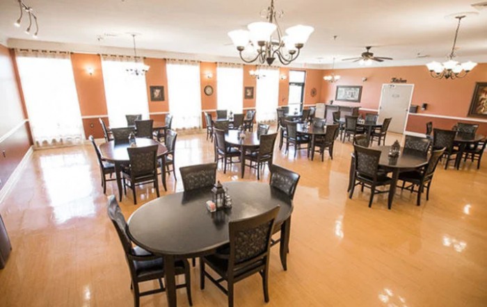 A well-lit dining area with multiple tables and chairs, featuring elegant chandeliers and wooden floors.