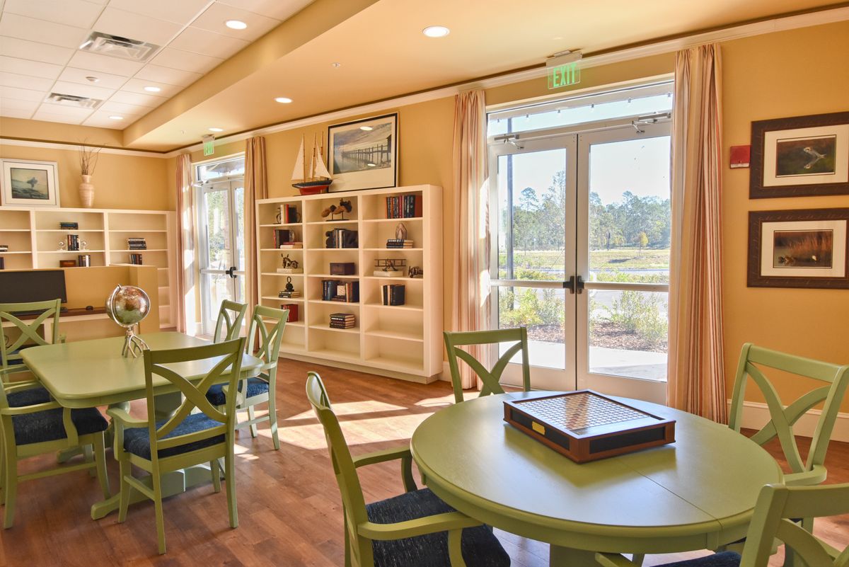 A cozy library interior with bookshelves, tables, and chairs bathed in sunlight.