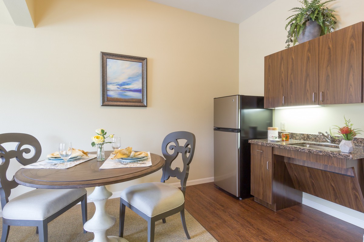 A cozy kitchen and dining area with a round table, chairs, fridge, and a decorative painting on the wall.