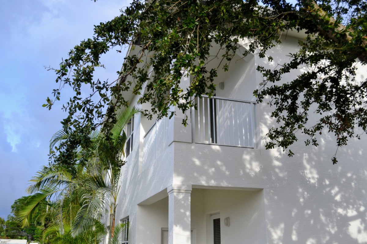 A white house with a balcony and trees casting shadows.