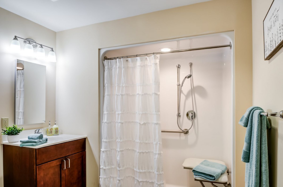 A bathroom with a shower, white curtain, vanity sink, mirror, and towels.