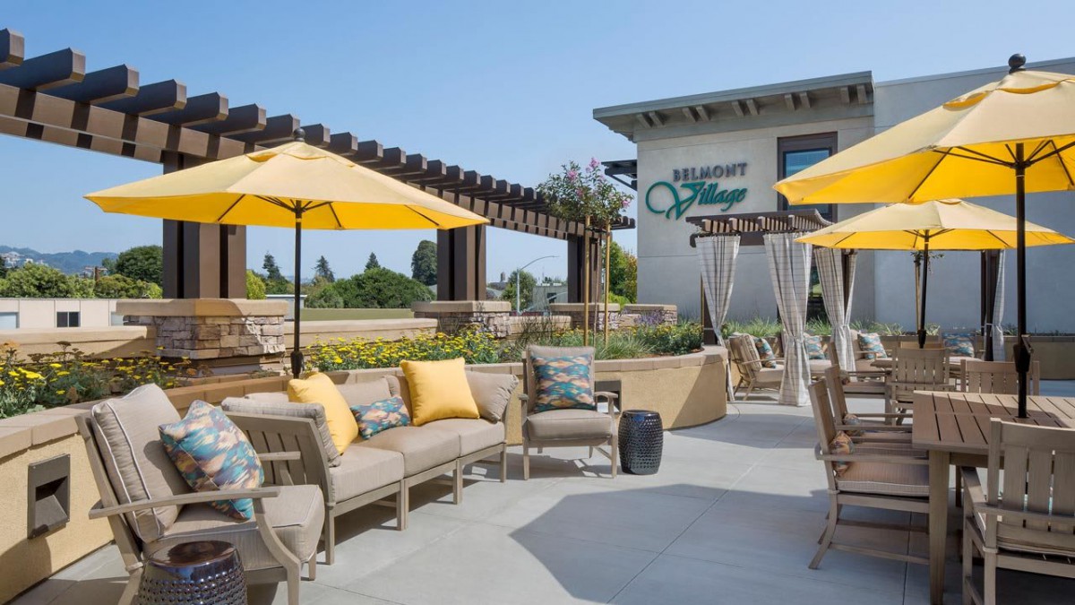 A comfortable outdoor seating area with yellow umbrellas and cushioned furniture, located near a building.