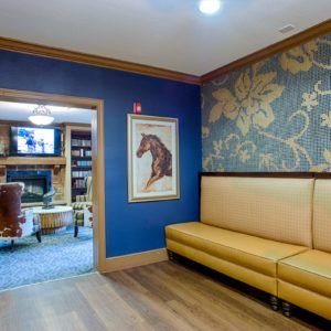 A cozy waiting area with a yellow bench and blue walls, decorated with floral wallpaper and artwork.