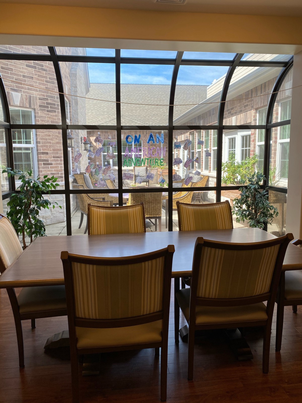 A stylish dining area with wooden furniture and indoor plants under a glass ceiling, flooded with natural light.