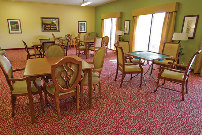 A well-lit dining room with several tables and chairs arranged on a patterned carpet.