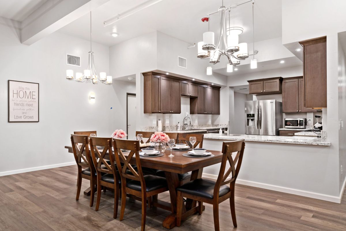 A modern open-concept dining room and kitchen with wooden furniture and elegant chandeliers.
