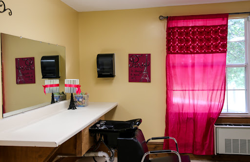 A cozy hair salon interior featuring a waiting area with a mirror, chairs, and vibrant red curtains.