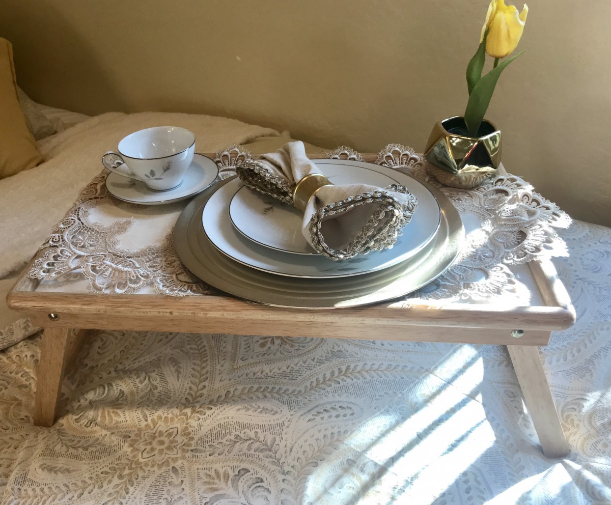 A cozy breakfast setup with a decorative tray featuring elegant dishware and a single yellow tulip in a vase.