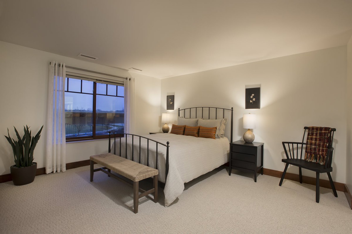 A cozy bedroom featuring a metal-framed bed, two side tables with lamps, a bench at the foot of the bed, and a large window.