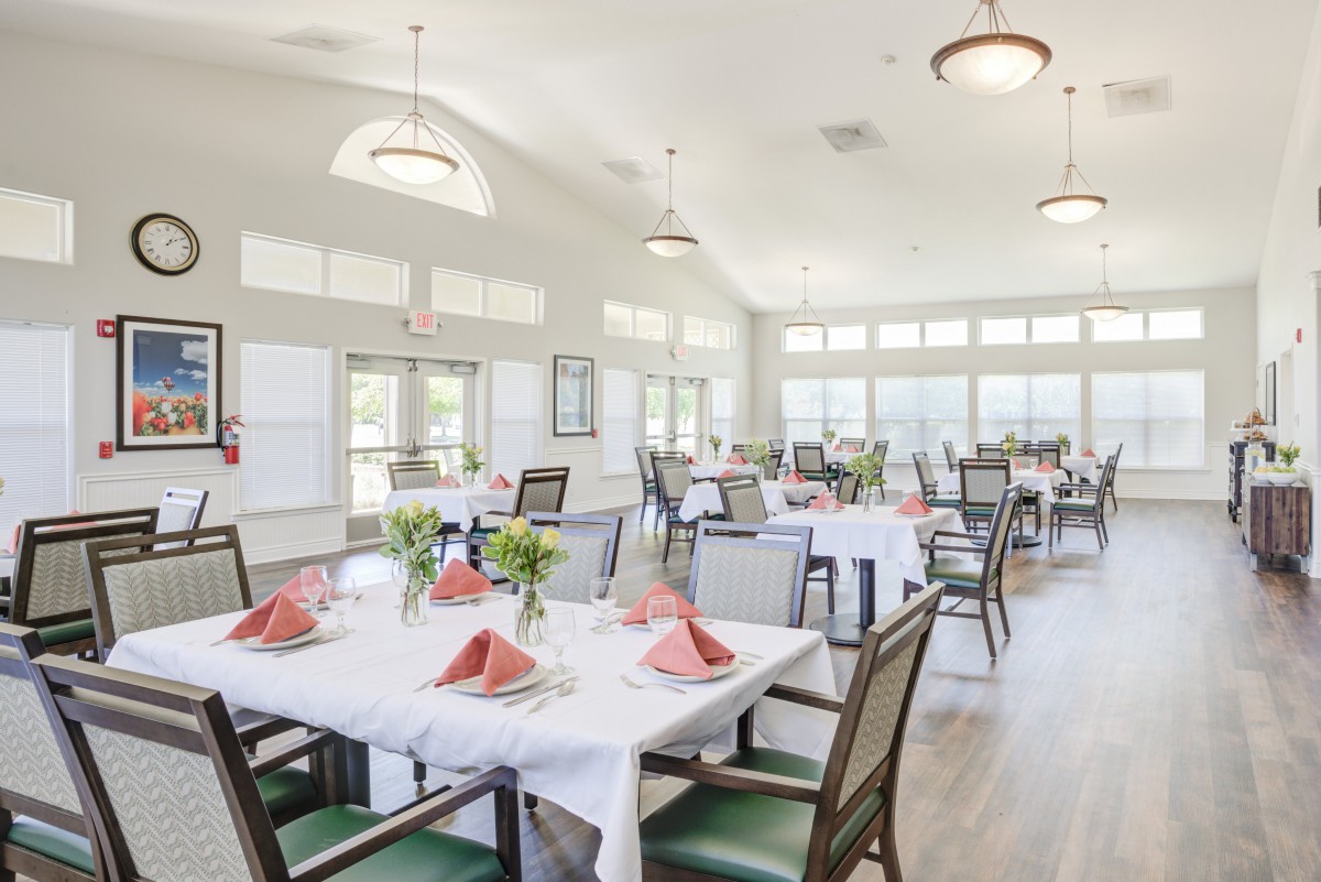 A bright dining area with neatly arranged tables and chairs, featuring white tablecloths and floral centerpieces.