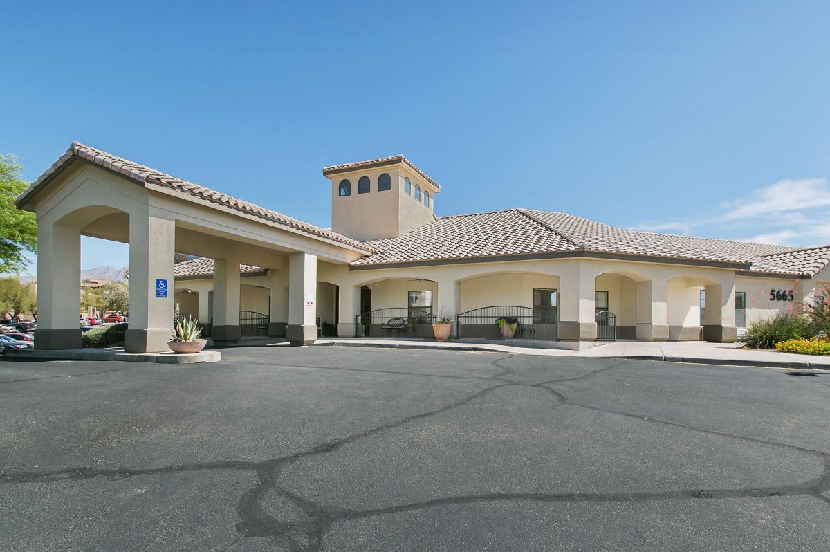 A hotel building with a prominent entrance and adjacent parking area under a clear blue sky.