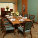 A well-decorated dining room with a large wooden table, surrounded by elegant chairs and set with white place settings.