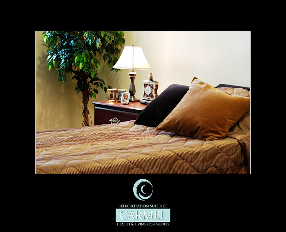 A cozy bedroom featuring a neatly made bed with pillows, a nightstand with a lamp, and decorative elements including framed photos and a plant.