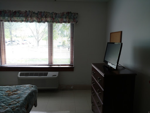 A simple bedroom featuring a dresser, television, and a large window allowing natural light.