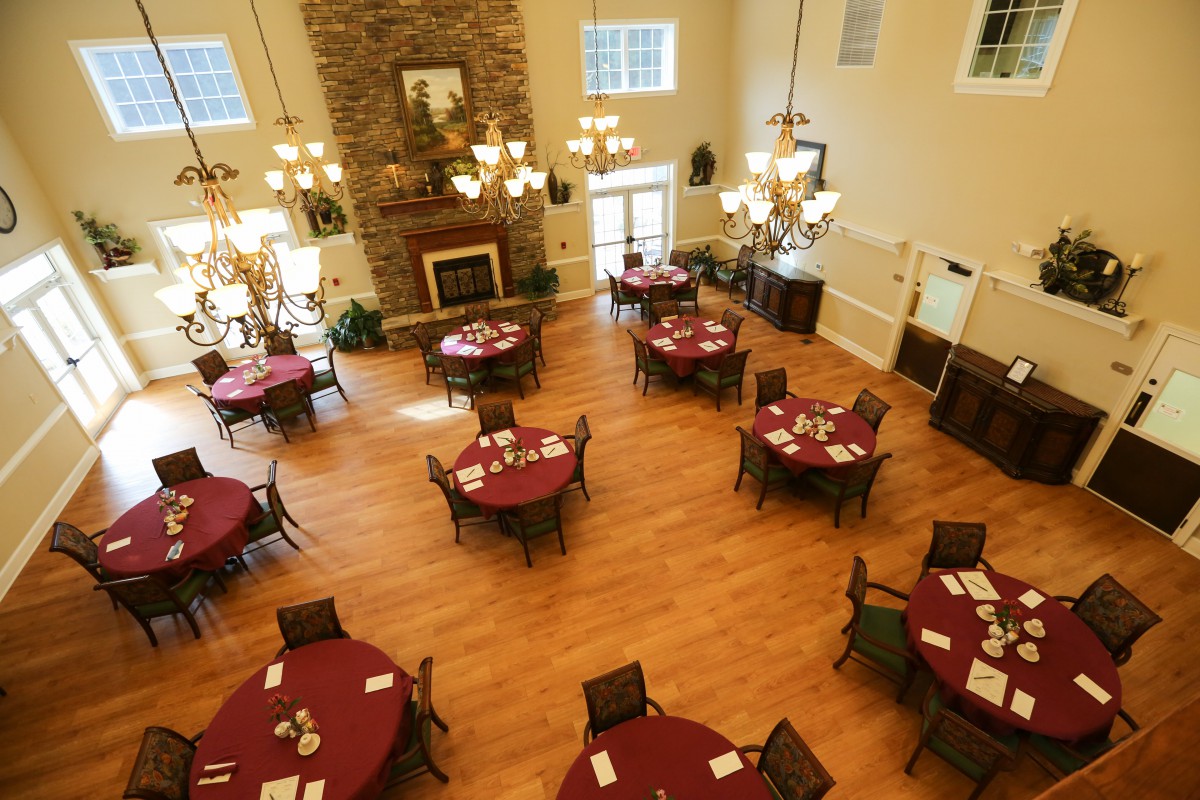 A spacious dining area with round tables and chairs, featuring a wooden floor and a grand fireplace.