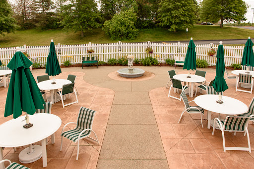 A serene outdoor seating area featuring tables and chairs with green umbrellas, surrounded by lush greenery.