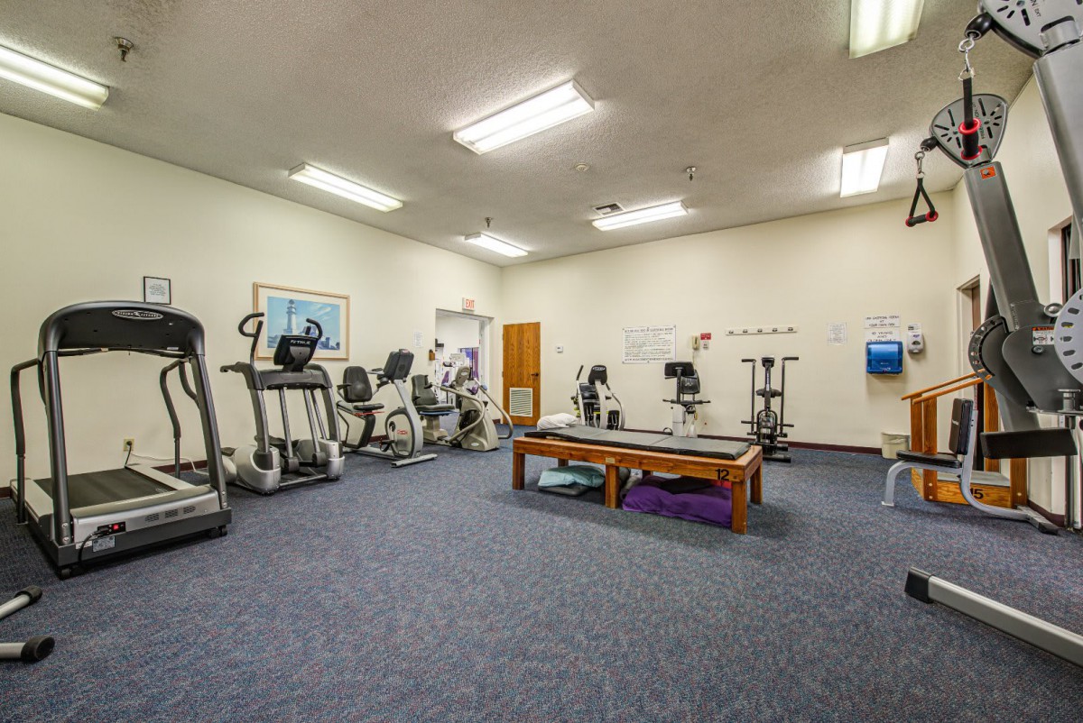 A well-equipped indoor gym with various exercise machines and a therapy area.