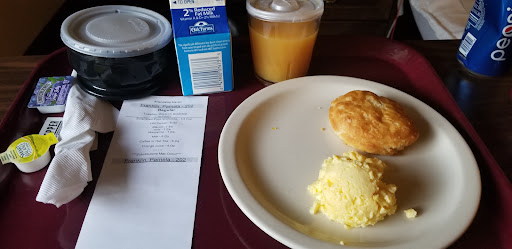 A simple breakfast setup featuring scrambled eggs, a biscuit, a carton of juice, and a receipt.