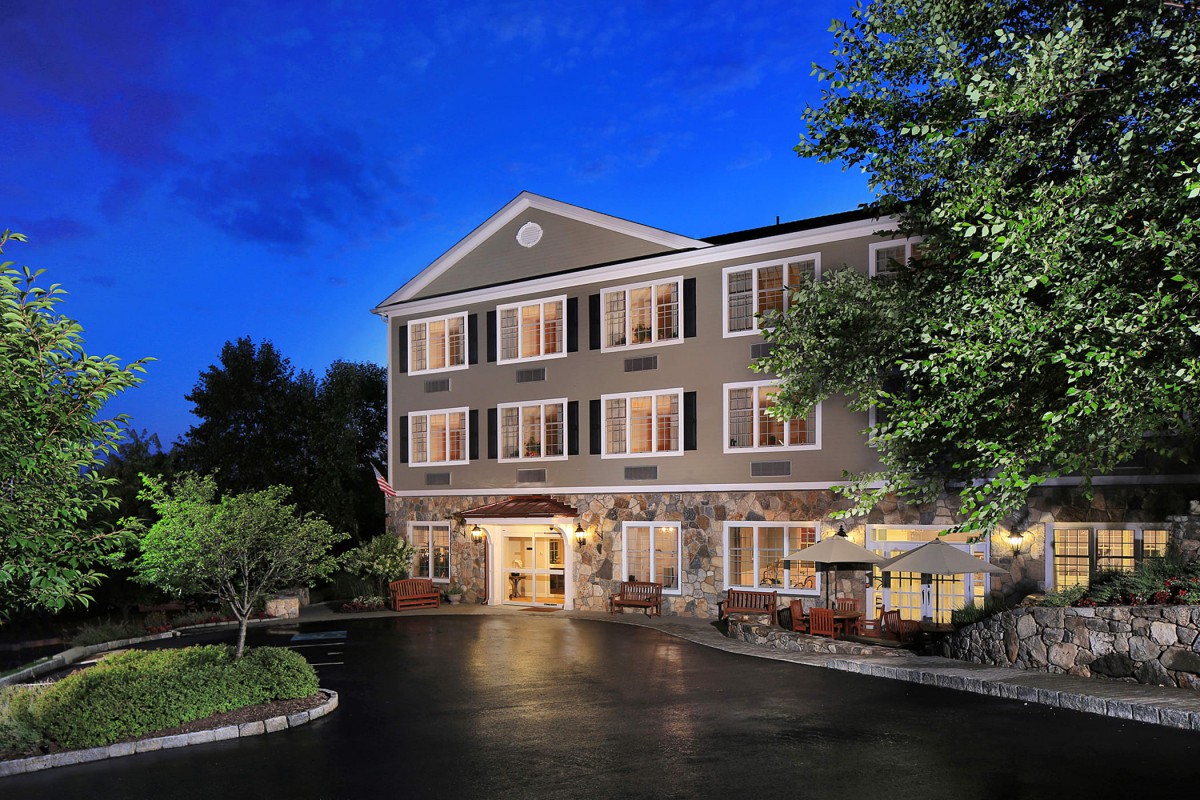 A cozy hotel building illuminated at night with surrounding trees and outdoor seating.