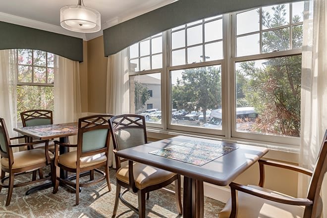 A well-lit dining area with wooden tables and chairs, featuring large windows that let in plenty of natural light.