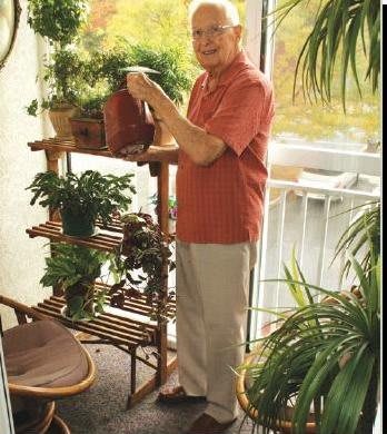 A senior man waters his indoor plants on a balcony.