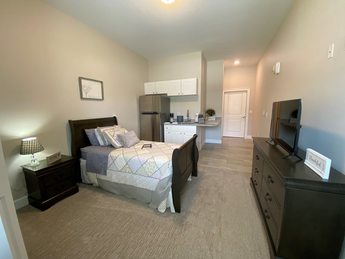 A cozy studio apartment with a single bed, kitchenette, and dresser.