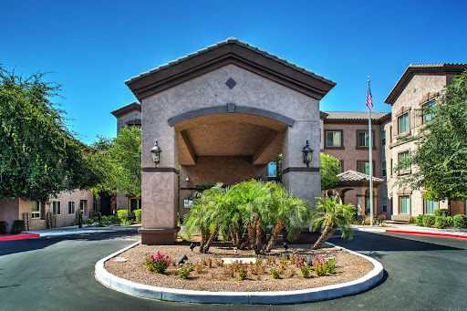 The welcoming entrance of a hotel surrounded by lush landscaping and clear blue skies.