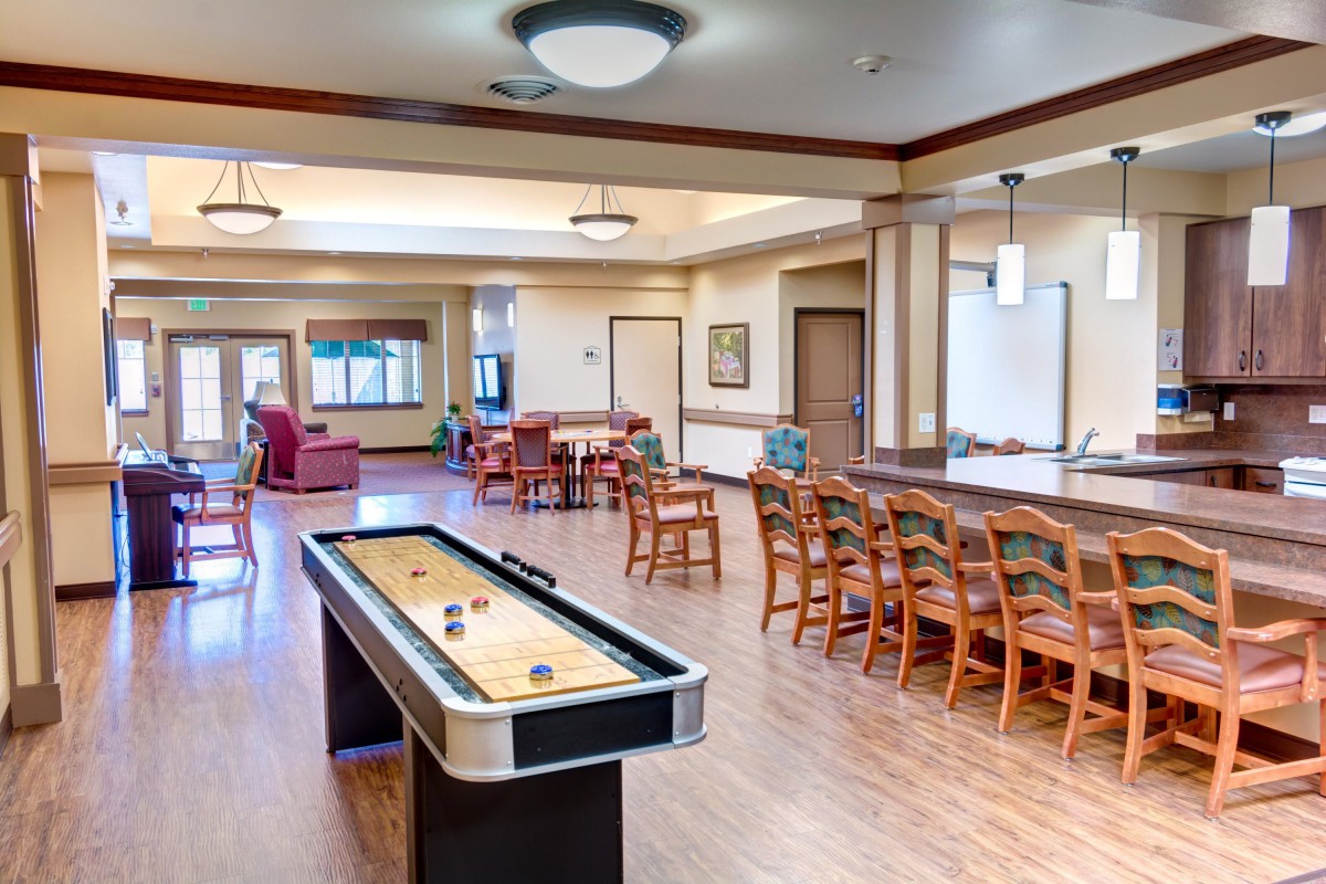 A spacious recreation room featuring a shuffleboard table, with ample seating and wooden flooring.