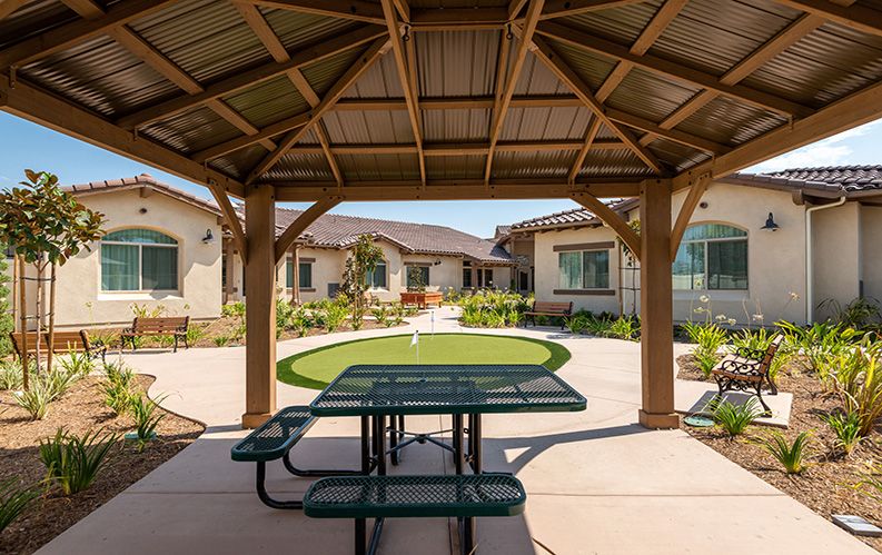 A covered outdoor area with a picnic table overlooking a landscaped garden in a residential setting.