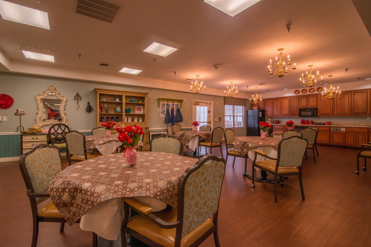 A cozy dining room with multiple tables and chairs, warmly lit with chandeliers.