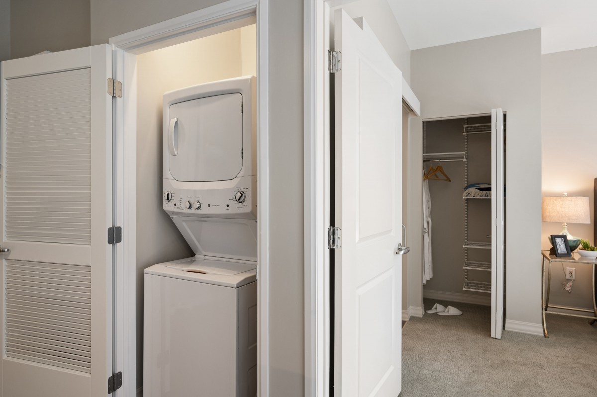 A small laundry closet with a stacked washer and dryer next to an open walk-in closet.