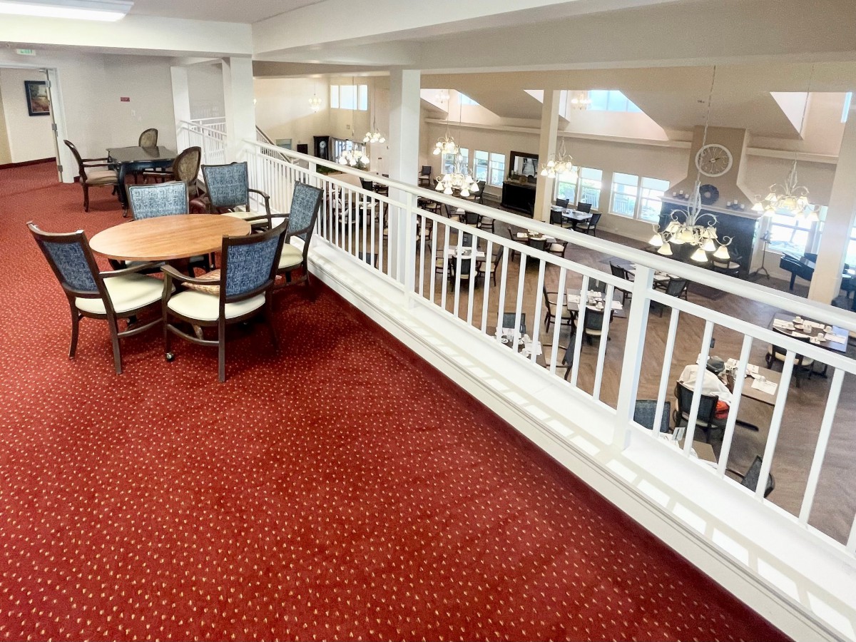 A spacious interior featuring a dining area with tables and chairs, decorated with a red carpet and white railing.