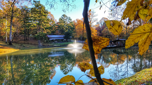 A tranquil autumn scene featuring a pond with a fountain, surrounded by colorful foliage.