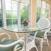 A sunlit room with a glass table and wicker chairs near large windows.