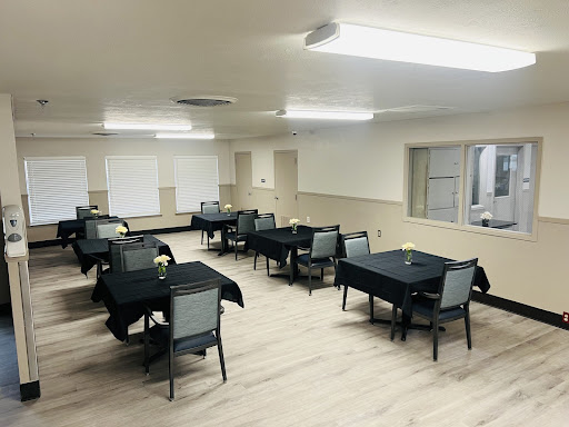 A spacious dining area with neatly arranged tables and chairs, featuring black tablecloths and bright overhead lighting.