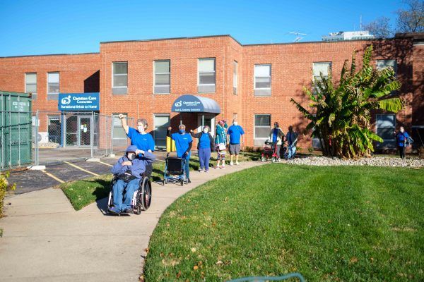 A group of people outside a brick building, with one person in a wheelchair on a sunny day.