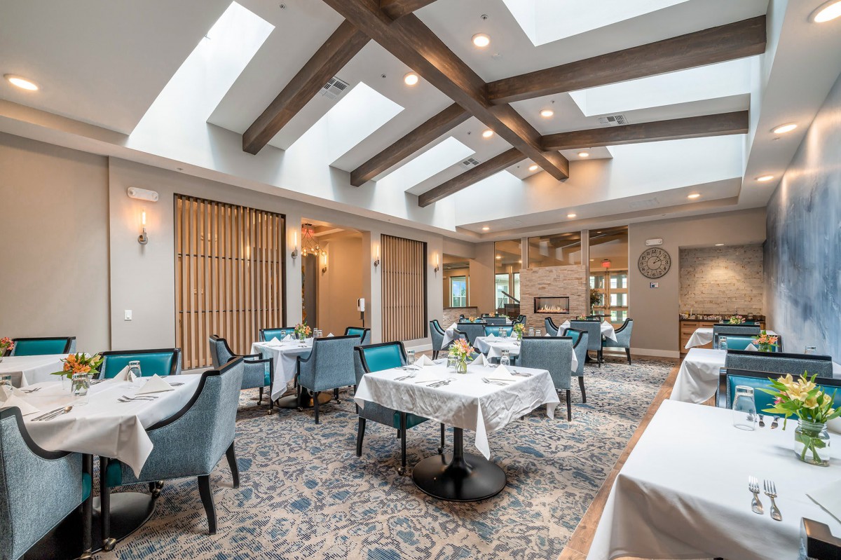 An elegant dining area featuring tables with white tablecloths, comfortable chairs, and natural light from skylights.