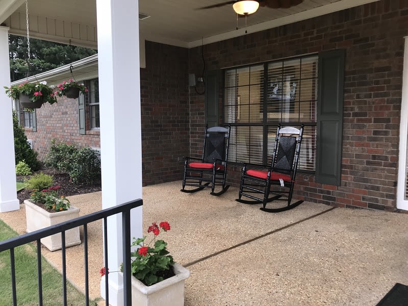 A cozy porch with two black rocking chairs and red cushions, surrounded by potted plants and a brick exterior.