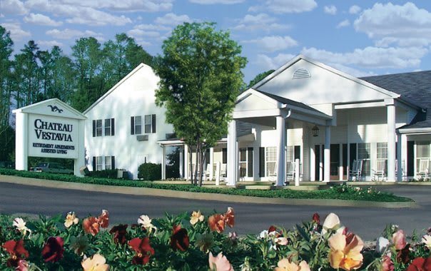 A suburban residential building surrounded by trees and colorful flowers.