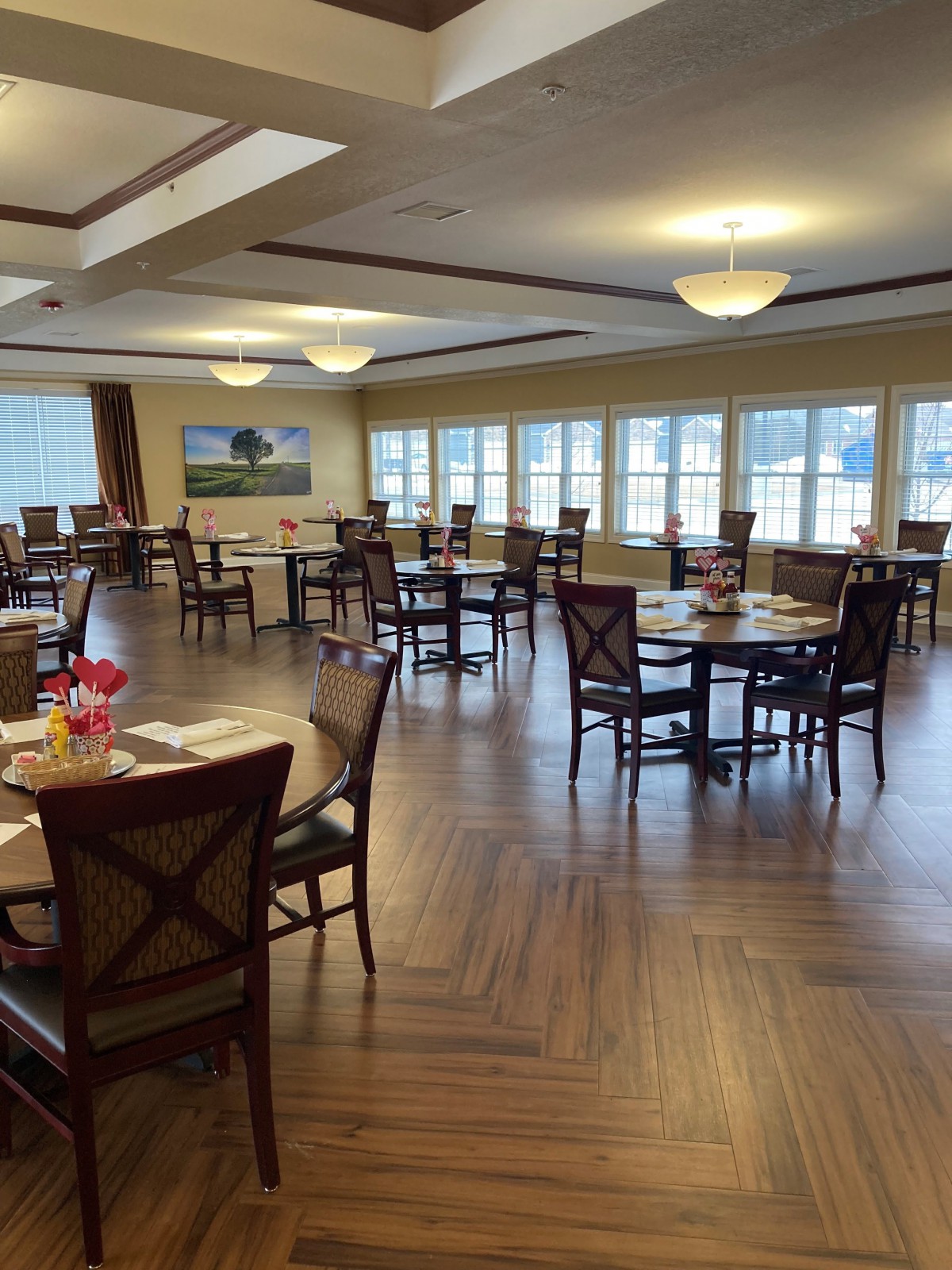 A spacious dining area with wooden tables and chairs, well-lit by large windows.