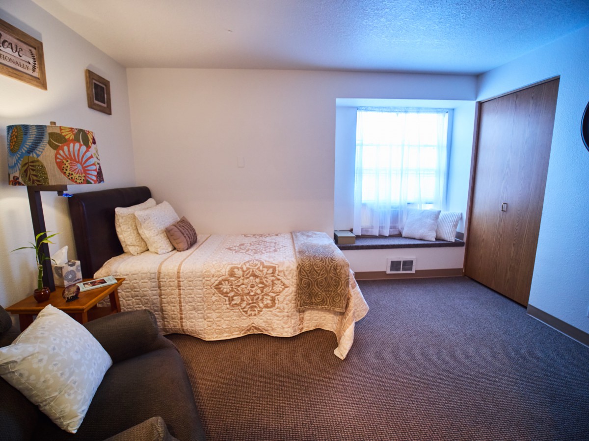 A cozy bedroom with a single bed and a large window letting in natural light.