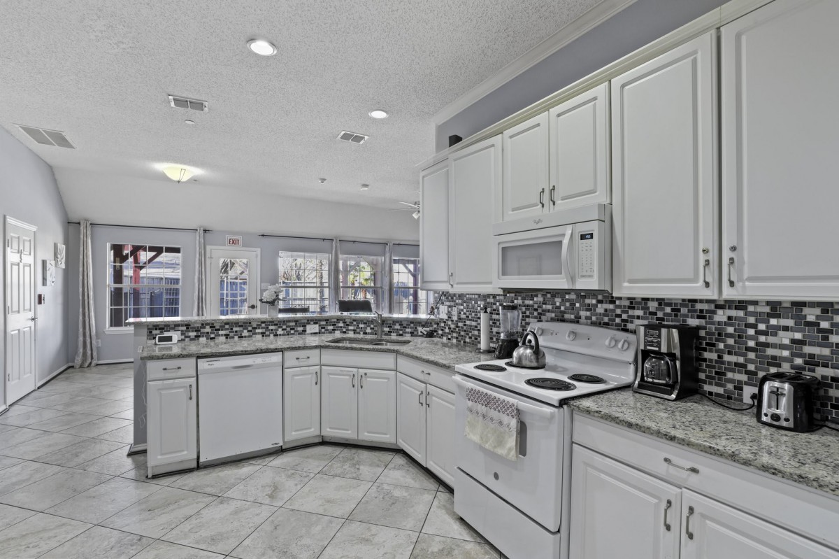 A modern kitchen with white cabinets and tiled flooring, featuring a sleek backsplash and bright lighting.