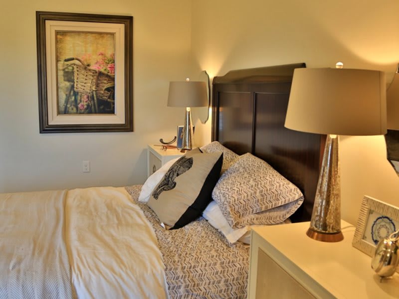A cozy bedroom with a neatly made bed, stylish lamps, and elegant artwork.