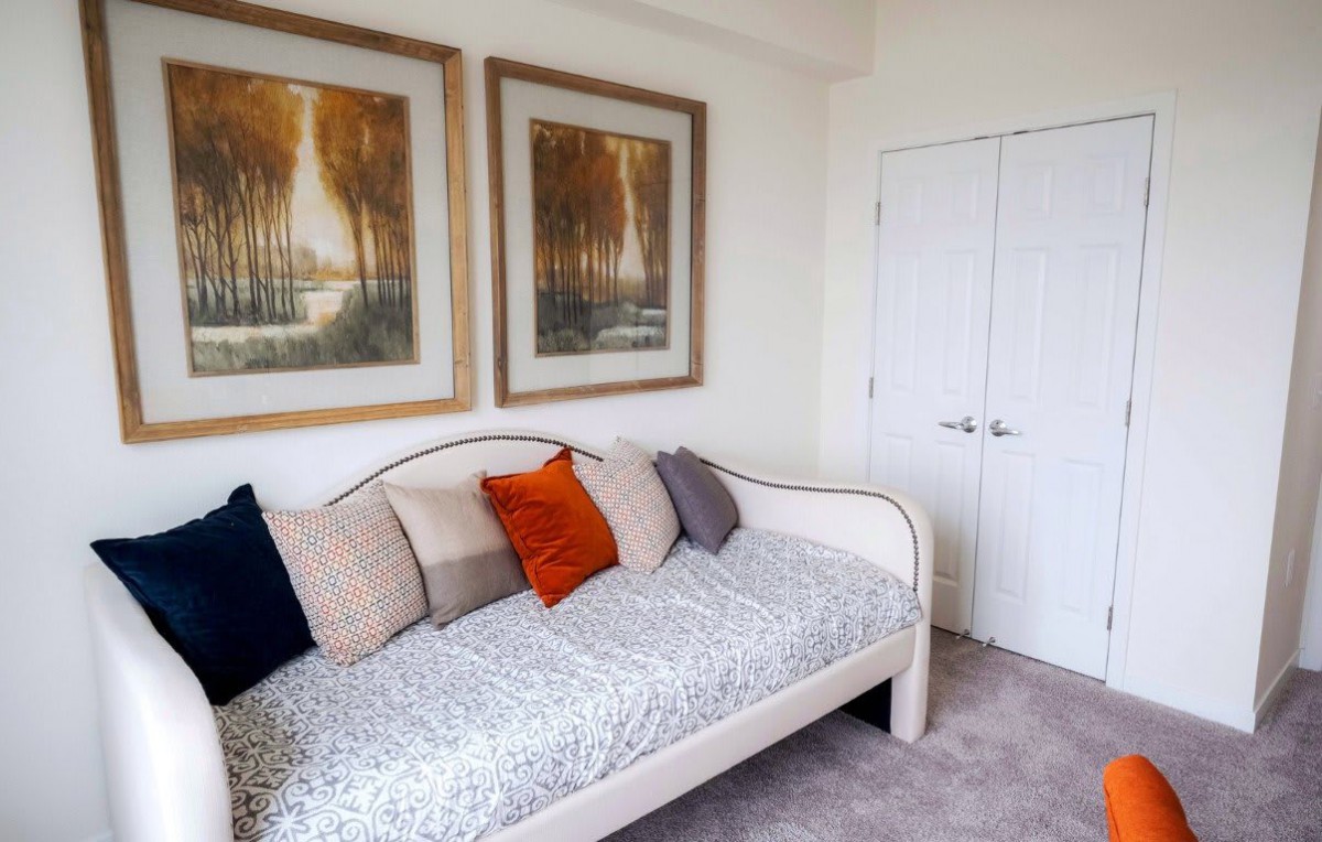 A cozy bedroom with a daybed adorned with colorful pillows and framed artwork on the wall.