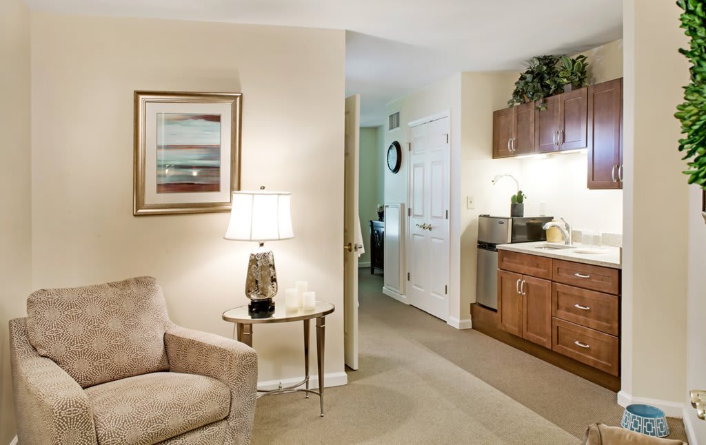 Cozy living room with a sofa, side table and lamp, leading to a kitchenette area.