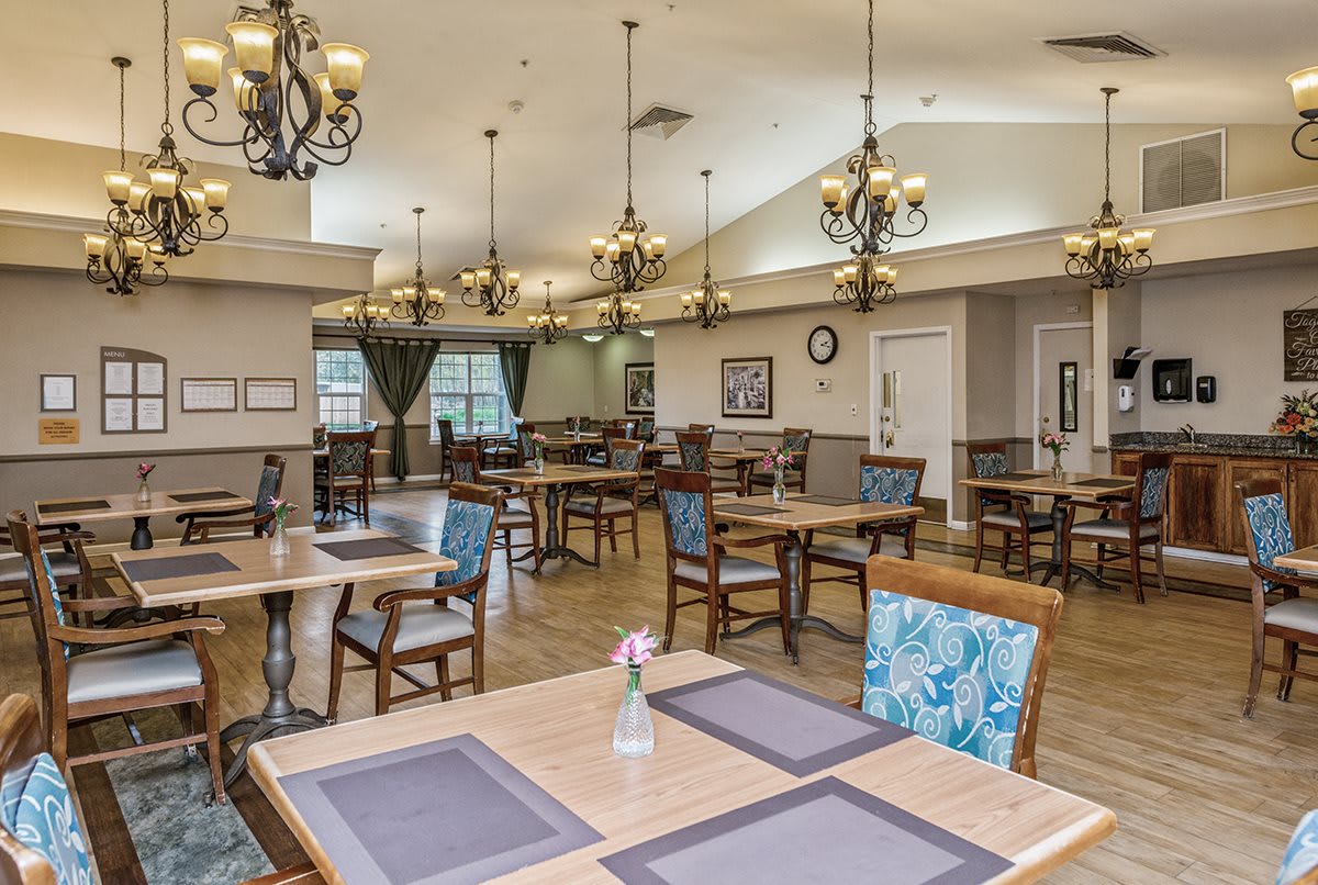A spacious dining room with elegant chandeliers, neatly arranged tables, and chairs.