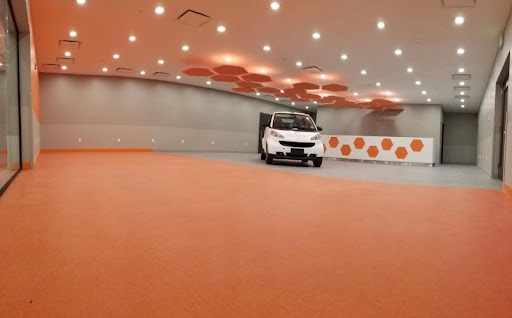 A sleek car parked in a modern interior with an orange flooring design and unique ceiling lights.