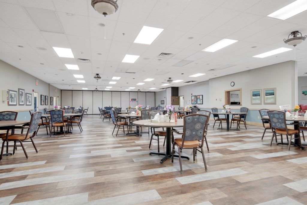 An empty dining hall with several tables and chairs arranged neatly under bright, overhead lighting.