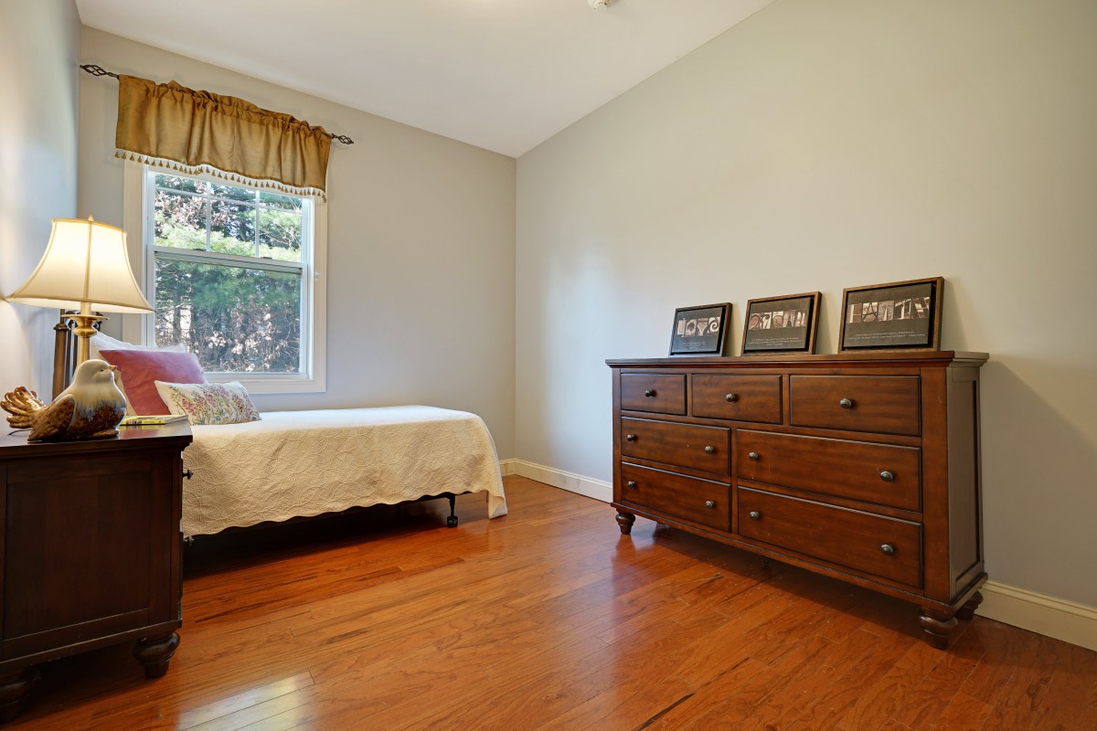A minimalist bedroom with wooden floors and furniture, including a bed and dresser.