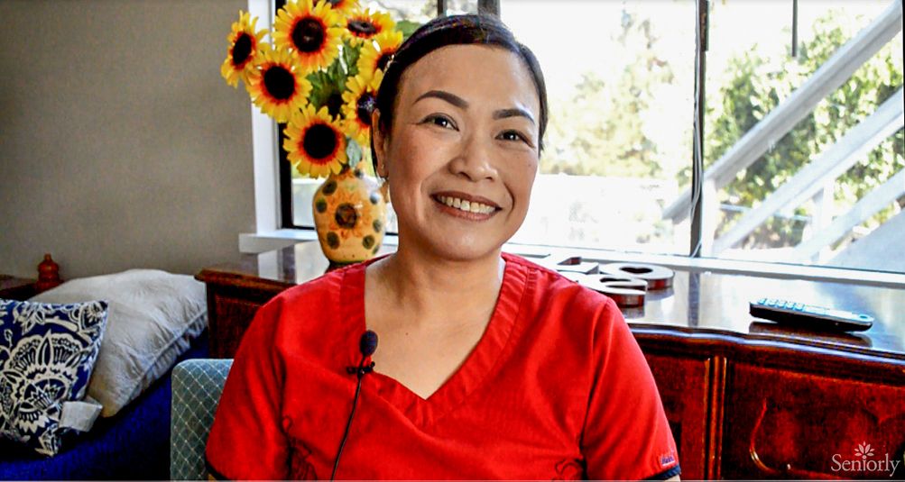 A woman in a red shirt smiling indoors with sunflowers in the background.